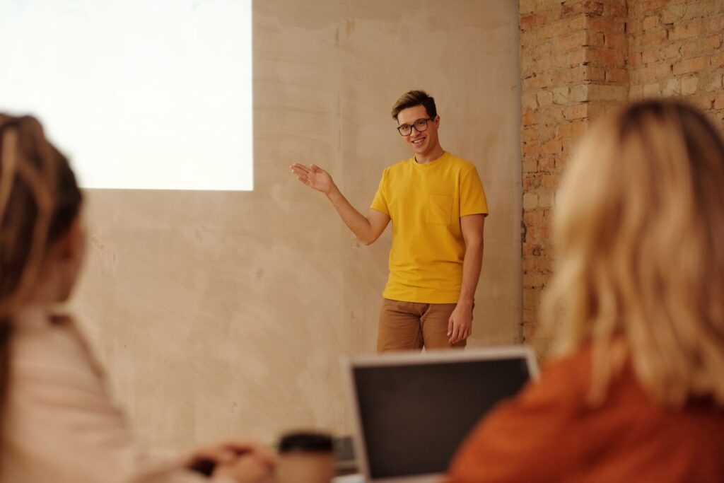 Young professional presenting in a modern office environment with a relaxed and engaging approach.